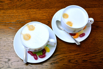 Two white cups of Cappuccino coffee with milk foam. In a saucer, on a wooden table.