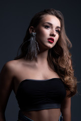 Close up beauty portrait of young beautiful woman with long curly hair wearing a black top and jeans. Studio shot.