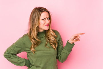 Fototapeta premium Young caucasian woman isolated on pink background smiling cheerfully pointing with forefinger away.