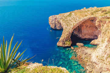 Blue Grotto in Malta. Pleasure boat with tourists runs. Natural arch window in rock - obrazy, fototapety, plakaty
