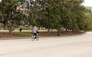 middle-aged woman with blond hair, walks or bike through paved park