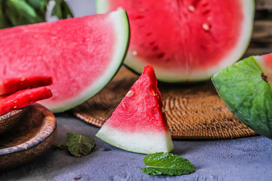 Photo of fresh watermelon with green leaves on wooden board over the table. Whole and sliced. Cutting board. Cut in halves. Dark background. Front view. Raw organic fruit. Image