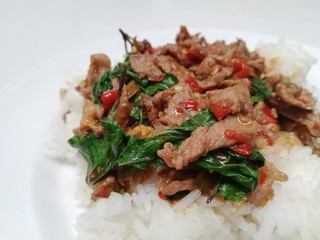 Popular spicy Thai dish, jasmin rice topped with stir fried beef with basil leaves, chilli and garic on white plate.