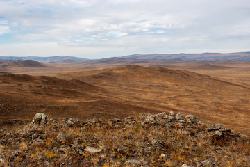 Beautiful steppe landscape with hills and stones. Brown tones. Clouds in the sky.