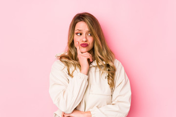 Young caucasian woman isolated on pink background looking sideways with doubtful and skeptical expression.