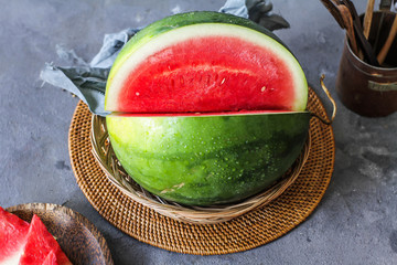 Photo of fresh watermelon with green leaves on wooden board over the table. Whole and sliced....