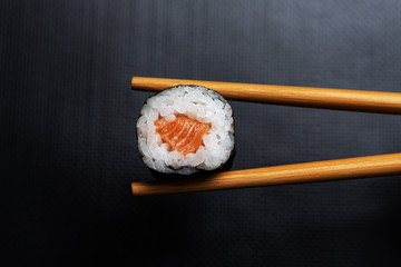 Stock photo of Maki sushi held with chopsticks on black background. Japanese cuisine composition.