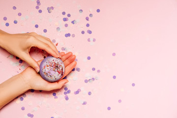 Flat lay composition with bath bombs in girls hand on pink background with festive confetti.