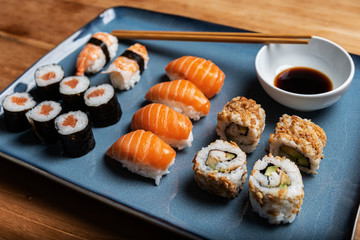 Stock photo of sushi plate with Maki, Nigiri and California Roll on blue plate. Close-up composition of an Asian gastronomic dish on wooden table.