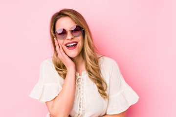 Young caucian woman with glasses isolated on pink background laughs happily and has fun keeping...