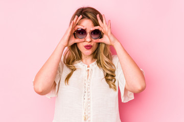 Young caucian woman with glasses isolated on pink background showing okay sign over eyes