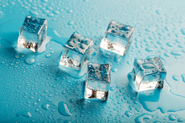 Ice cubes with water drops scattered on a blue background, top view.