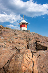 Republic of Finland, Helsinki, Suomenlinna: Abandoned beautiful red white striped lighthouse on rocky cliff from below with blue sky in the background - concept nautical danger navigation travel