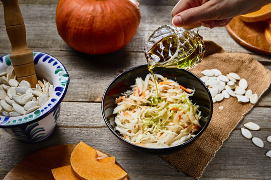 hand with Cold pressed Pumpkin seed oil in a glass over sauerkraut. pampkin seeds in pounder