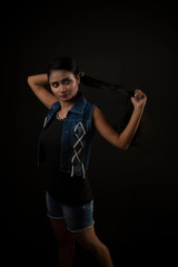 Fashion portrait of an young and attractive Indian Bengali brunette girl with tee shirt and blue western jacket tying hair in front of a black studio background. Indian fashion portrait and lifestyle.