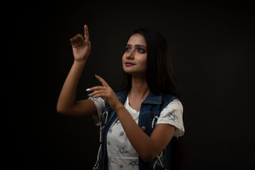Fashion portrait of an young and attractive Indian Bengali brunette girl with tee shirt and blue western jacket in front of a black studio background. Indian fashion portrait and lifestyle.