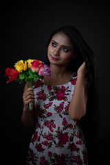 Fashion portrait of an young and attractive Indian Bengali brunette girl with floral western dress with flowers in front of a black studio background. Indian fashion portrait and lifestyle.