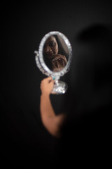 Fashion portrait of an young and attractive Indian Bengali brunette girl with floral western dress looking through mirror in front of a black studio background. Indian fashion portrait and lifestyle.