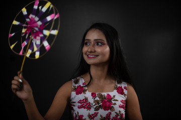 Naklejka premium Fashion portrait of an young and attractive Indian Bengali brunette girl with floral western dress with pinwheel in front of a black studio background. Indian fashion portrait and lifestyle.