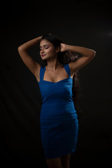 Fashion portrait of an young and attractive Indian Bengali brunette girl with blue western dress in front of a black studio background. Indian fashion portrait and lifestyle.