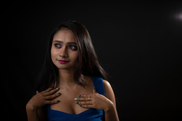 Naklejka premium Fashion portrait of an young and attractive Indian Bengali brunette girl with blue western dress in front of a black studio background. Indian fashion portrait and lifestyle.