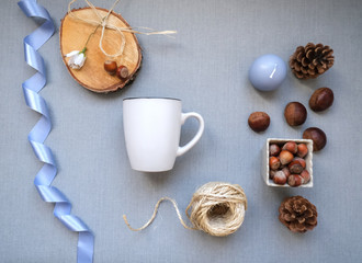 Flat lay top view autumn background concept to display your art, blue ribbon, blank cup, jute rope spool, candle, sweet chestnut, pine cones on the light grey background