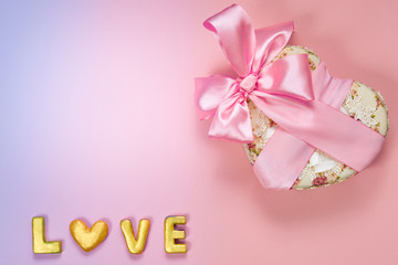 Heart shaped Valentines Day gift box with pink curved ribbon and gold word love on paper background. Top view, flat lay.