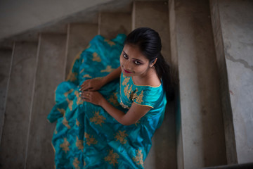 Fototapeta premium Top view fashion portrait of an young and attractive Indian Bengali brunette girl in Indian traditional dress sitting on staircase. Indian fashion portrait and lifestyle.