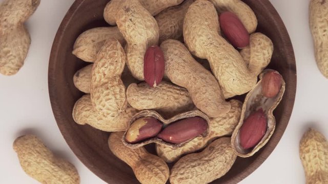 Bunch of peanuts in bowl rotating on white background. Top view Close up. Arachis hypogaea