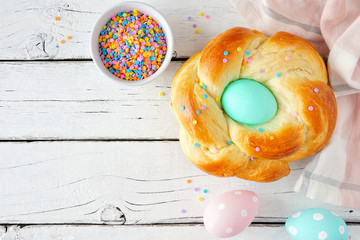 Homemade braided Easter bread with colorful egg. Top view table scene with a white wood background.