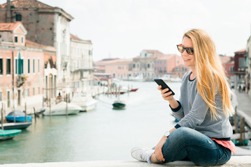 Fototapeta na wymiar Young female traveler using smartphone on the bridge in Murano island in Venice, Italy