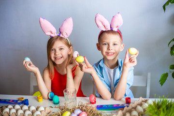 cute children 7-9 years old, wear bunny ears on their heads and paint Easter eggs on a blue background