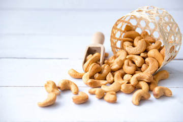 Roasted tasty cashew nuts in wooden spoon in bowl on a white  wooden table, isolated background...