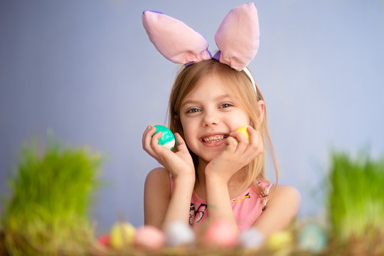 Cute little baby wears bunny ears on Easter day. cute little girl holding easter eggs in her hands and smiling. blue background