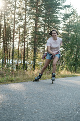 Happy, smiling woman is roller skating, at high speed, on the road, on a summer day. Active holidays.