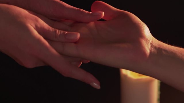 Women's hands predict on the man's palm, isolated on a black background next to a burning candle. The concept of palmistry, magic and clairvoyance. A woman reads lines on males hand