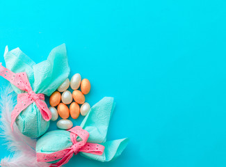 Egg gift in green paper packaging and with pink ribbon Easter Bunny wrap idea. Chocolate dragee white and gold color, multicolor colorful feathers. Minimal concept. Flat lay, Copy space, top view