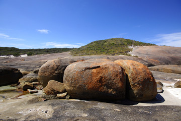 Red, grey and brown granite rocks in front of a green hill, Western Australia, southwest coast
