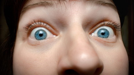 Face of a caucasian woman with blue eyes expressing curiosity and surprise with horror close up...