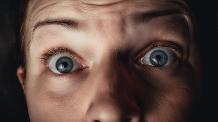 Face of a caucasian woman with blue eyes expressing fear and surprise with horror and long hair on a dark background