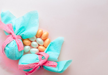 Egg gift in green paper packaging and with pink ribbon Easter Bunny wrap idea. Chocolate dragee white and gold color, multicolor colorful feathers. Minimal concept. Flat lay, Copy space, top view