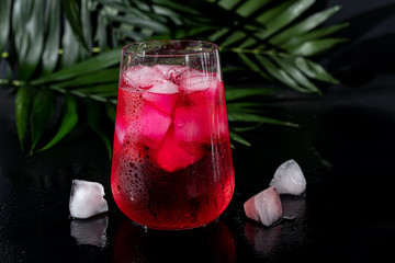 Raspberry-barberry drink in a transparent glass with ice. The drink is poured into a glass. Added...