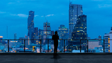 Businessman standing using smart phone on open roof top balcony watching city night view.Business with ambition and vision concept.