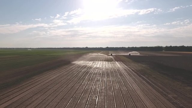 Tractor works on field of lettuce plantation outdoor, sprinkle spray field, machinery for watering, irrigation. Aerial footage
