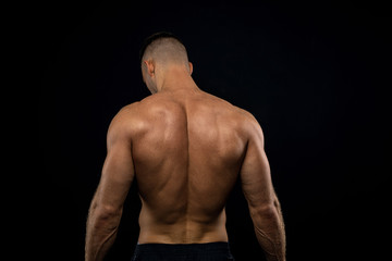 Fototapeta na wymiar powerful muscular athlete shows off his back beside black wall