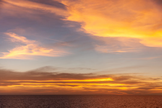 Tasman Sea, Australai - December 10, 2009: Red sunset with brown to orange and yellow clouds in light to dark blue sky over dark red sea. 