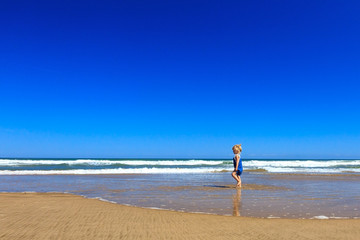 The girl is walking along the beach on a sunny day.