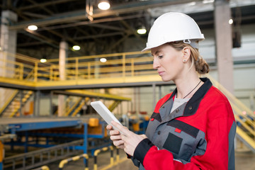 Horizontal portrait shot of professional female factory worker wearing uniform using tablet PC