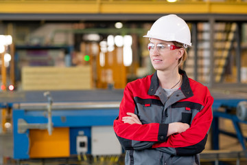 Horizontal medium portrait of attractive Caucasian female factory engineer standing with arms crossed looking away smiling