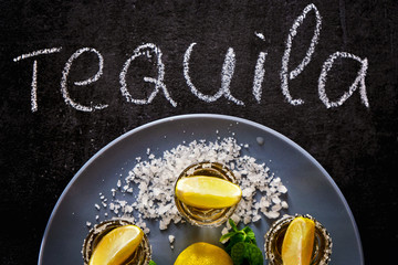 Gold tequila shot with lime and sea salt on grey plate.